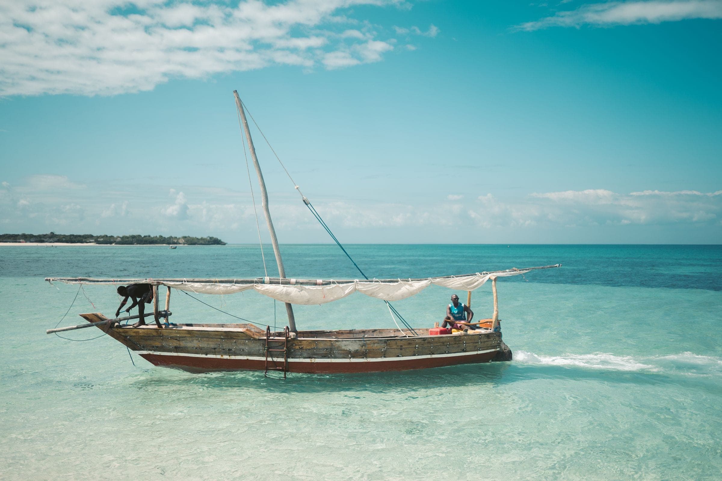 Two fishermen sailing a dhow on clear water off Zanzibar