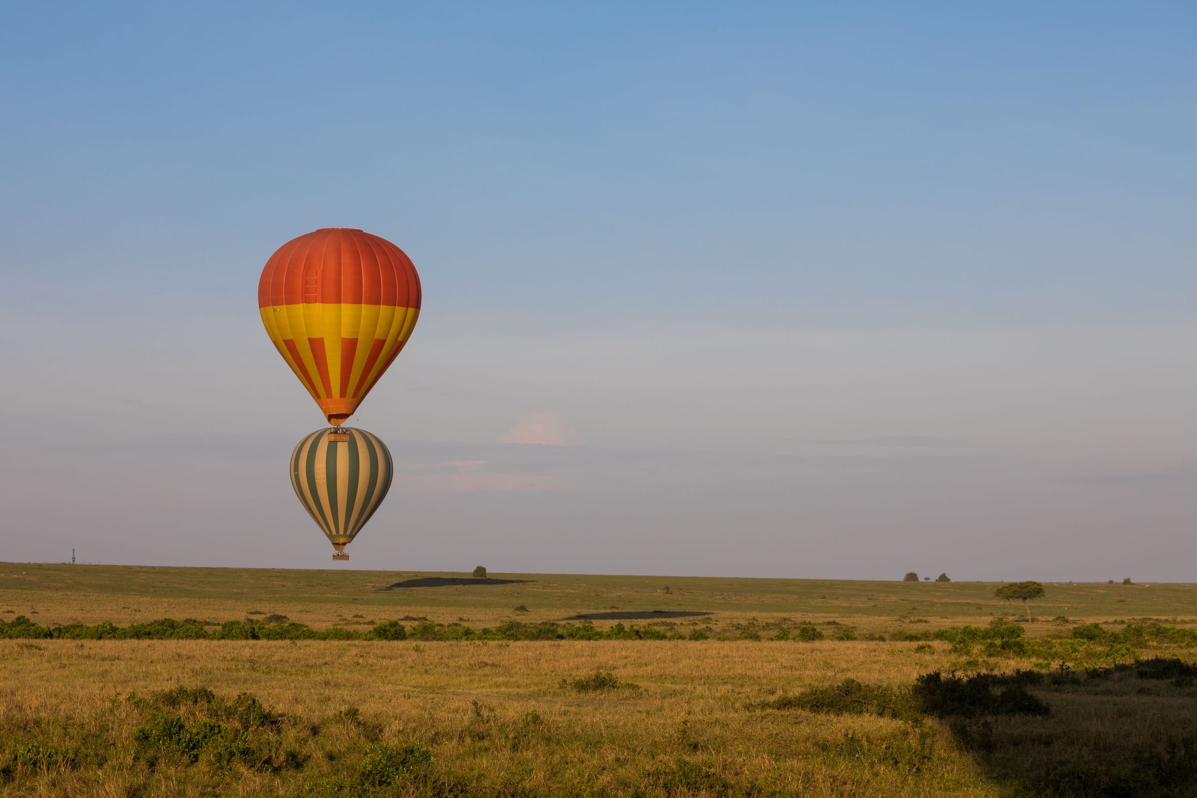 A hot-air balloon floating above open plains at sunrise