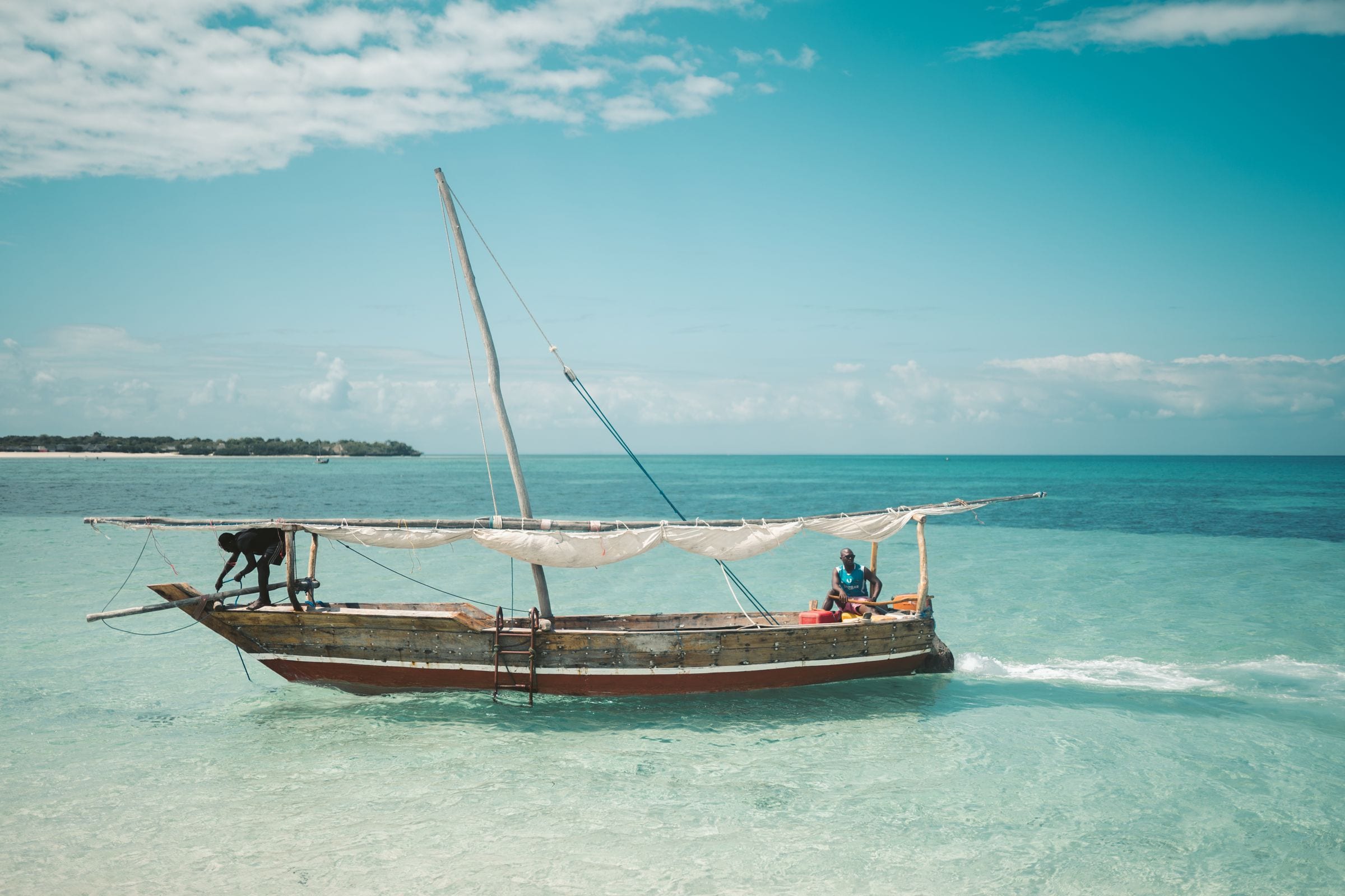 Two fishermen sailing a dhow on clear water off Zanzibar